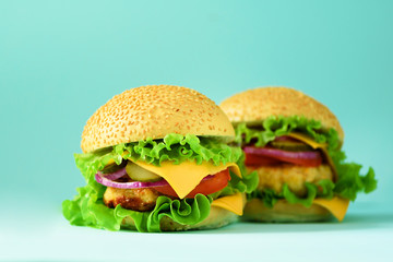 Unhealthy burgers with beef, cheese, lettuce, onion, tomatoes on blue background. Take away meal. Unhealthy diet concept. Copy space