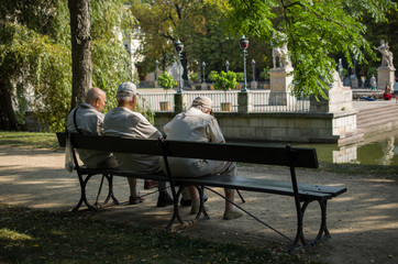 Old men sitting on a wooden bench in park and talking to each other
