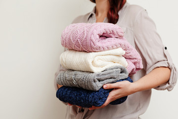 Girl with pile of knitted winter clothes in her hands on white background