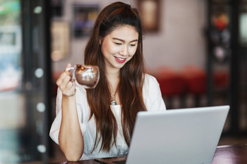 Beautiful Attractive Business Asian woman working with laptop holding coffee and looking in monitor smile and have positive emotional feeling so happiness,Business Startup Concept