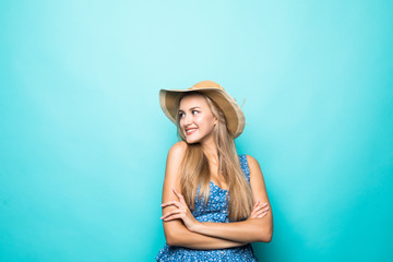 Portrait of a smiling young woman in straw hat standing with arms folded and looking away at copyspace isolated over blue background