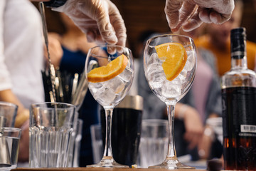 hands of the barman and two glasses with ice and orange slices