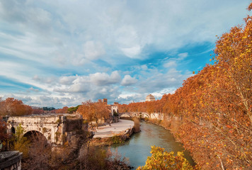 Autumn and foliage in Rome. Red and yellow leaves near Tiber Island with two ancient bridges and beautiful sky, in the city historic center