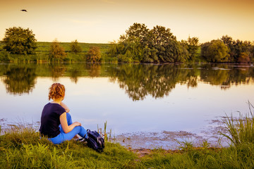 The girl is sitting by the river in the evening and admiring nature_