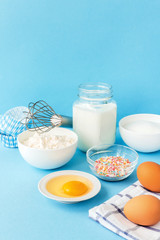 Eggs, flour, milk, sugar, and various ingredients for making pastry homemade pastry on a blue background with copy space