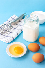 Eggs, flour, milk, sugar, and various ingredients for making pastry homemade pastry on a blue background with copy space