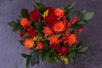 Fototapeta na wymiar Autumn bouquet with red and orange roses together with red berries and green leaves