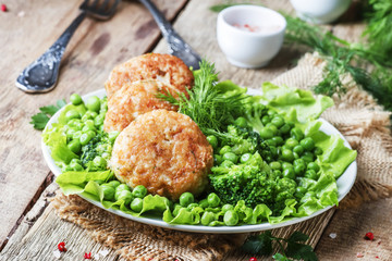 Fish cutlets or meatballs from cod and pike perch with a garnish of green peas and broccoli, rustic style, selective focus
