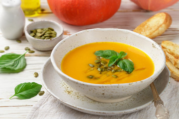 Dietary vegetarian pumpkin cream soup puree with olive oil, seeds and Basil on a light wooden table in a white plate