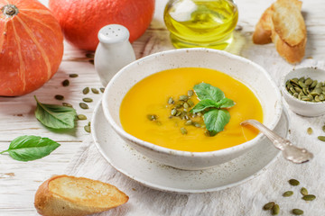 Dietary vegetarian pumpkin cream soup puree with olive oil, seeds and Basil on a light wooden table in a white plate