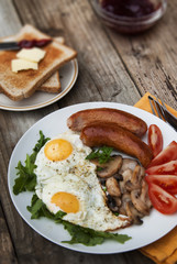 English breakfast. Eggs, sausages, mushrooms, tomatoes, toast bread. Eating tasy food over rustic wooden table.