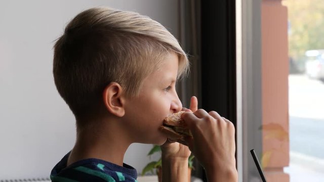Boy kid portrait in a cafe bistro sit eating biting a big tasty bagel sandwich for the lunch