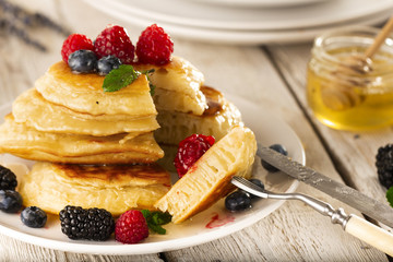 Pancakes with forest fruits berries on white table.