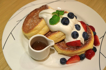 Delicious Souffle Pancake with Maple Syrup, Fresh Whipped Cream and Mix Berries Served on white Plate 