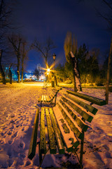 Night shot with a wooden bench in the park covered in snow