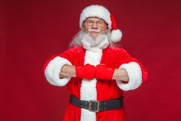 Christmas. Santa Claus with red bandages wound on his hands for boxing imitates kicks. Kickboxing, karate, boxing. Isolated on red background.