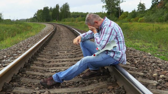 Depressed disabled man with crutches sitting on railway and crying