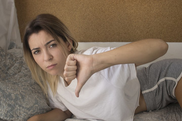 young girl in bed gesturing thumbs down - obrazy, fototapety, plakaty