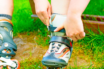 The skater binds the roller skates on the bench. Closeup inline skates in the green grass. In-line...