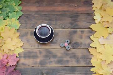 A cup of tea and a wooden spinner among the many yellowing fallen autumn leaves on the background...