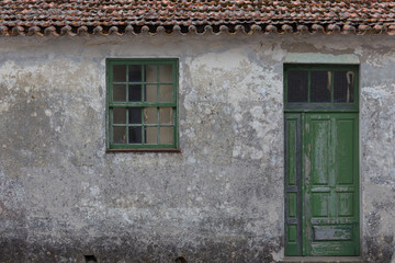 Fototapeta na wymiar Old wooden green door on concrete dilapidated wall with window on the side