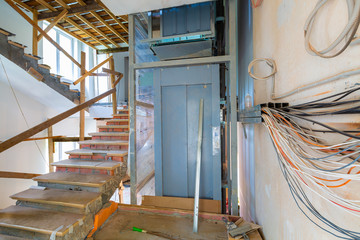 Wall  with wires, stairs with temporary wooden railing and elevator in an apartment is during on the construction, remodeling, rebuilding and renovation.  © Zakhar Marunov
