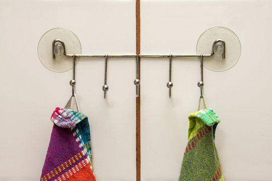 Two colourful towels hanging on a hooks with suction cups in a kitchen