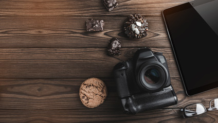 Top view of photographer concept with digital camera, tablet, glasses and cooky on wooden background with copy space