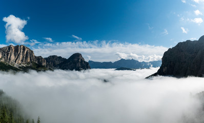 panorama mountain landscape in the Val Gardena in the Italian Dolomites with mountain peaks and thick cloud cover in the valleys underneath a blue sky in late autumn