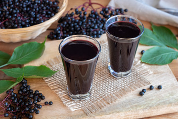 Fototapeta na wymiar Two glasses of black elder syrup with fresh elderberries