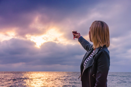 Girl holding a glass with wine uring the sunset on the sea