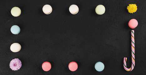Colorful macarons, lollipop and flowers in the form of a frame on black stone table. Top view with copy space for text