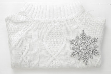 Obraz premium Knitted winter white sweater and snowflake decoration on white wooden background. top view