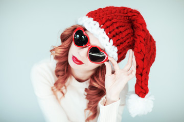 Santas little helper. Beautiful happy young woman with a santa claus hat, perfect make up, red...