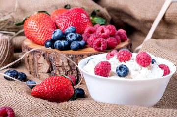 Berries of raspberries, strawberries, blueberries on a a baggy background, cottage cheese with berries in a white plate. Proper nutrition
