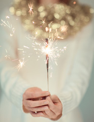 Beautiful woman hands holding sparkler lights, cozy, bright winter sweater with golden christmas...