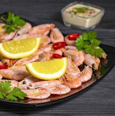 sauce and shrimp with pepper, lemon and greens on a black plate