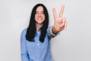 Beautiful young happy smiling girl in blue shirt showing victopy sing with her hand. Peace concept....