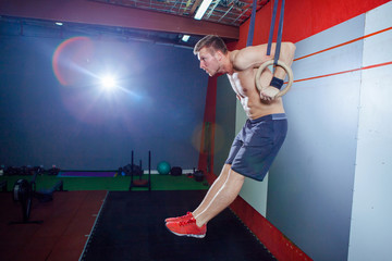 Muscle-up exercise young man doing intense cross fit workout at the gym on gymnastic rings.