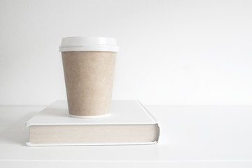 Hot drink mug with some coffee on a book. Exam period for education time and study concept against an empty white copy space background.