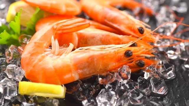 Shrimps. Fresh prawns rotated on a black background. Seafood on crashed ice with herbs. Healthy food, cooking. Rotation. Slow motion 4K UHD video 3840x2160