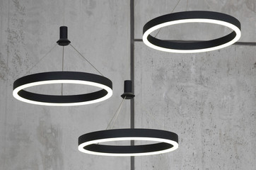 Unusual light sources hang on the background of a marble wall. Lamps in the form of a luminous ring