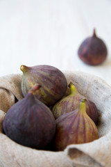 Fresh figs in a bowl on white wooden background, side view. Selective focus.