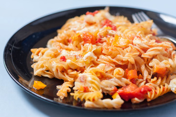 A plate of roasted vegetable pasta bake on a pale blue surface