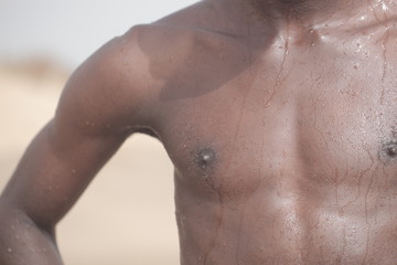 human body - close up of a fit african male torso, outdoors on a sunny day, with water drops