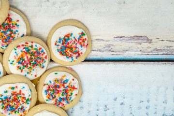 Vanilla white frosted homemade sugar cookies piled on a blue wooden background. Birthday rainbow...