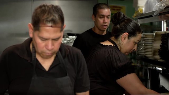 Cooks of hispanic descent preparing food in a Mexican food restaurant while the manager comes in to talk to them