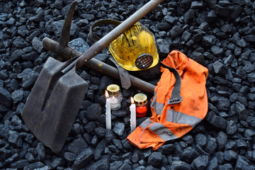 Vigil light, candle with the miner belongings (helmet, pickaxe, shovel, vest, belt) - obrazy, fototapety, plakaty