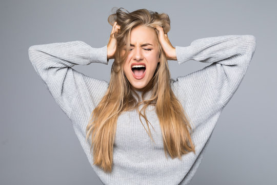 Portrait of a frustrated angry woman screaming out loud and pulling her hair out isolated on the gray background