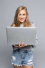 Young happy smiling woman in casual clothes holding laptop and sending email to her best friend isolated on gray background